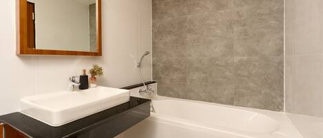Un baño moderno con lavamanos blanco, encimera negra y una bañera grande.