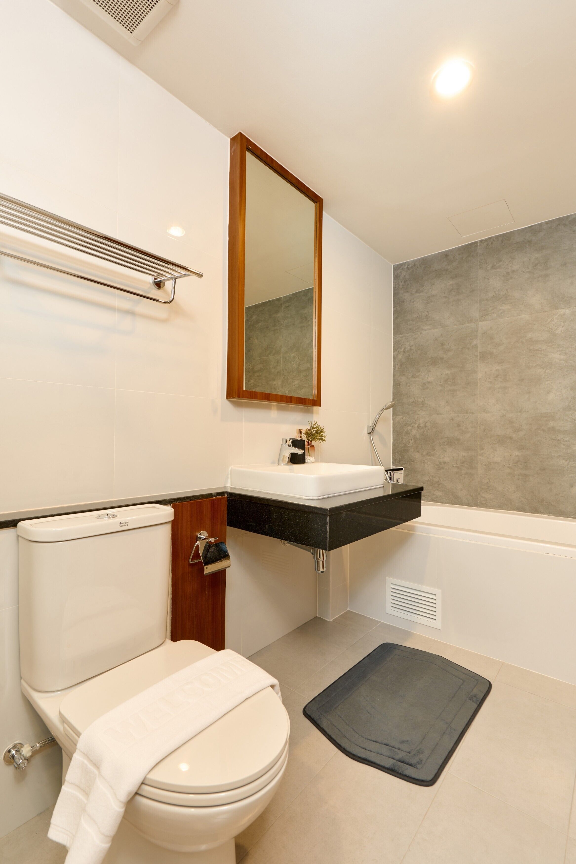 A modern bathroom with a toilet, sink, mirror, and bathtub.