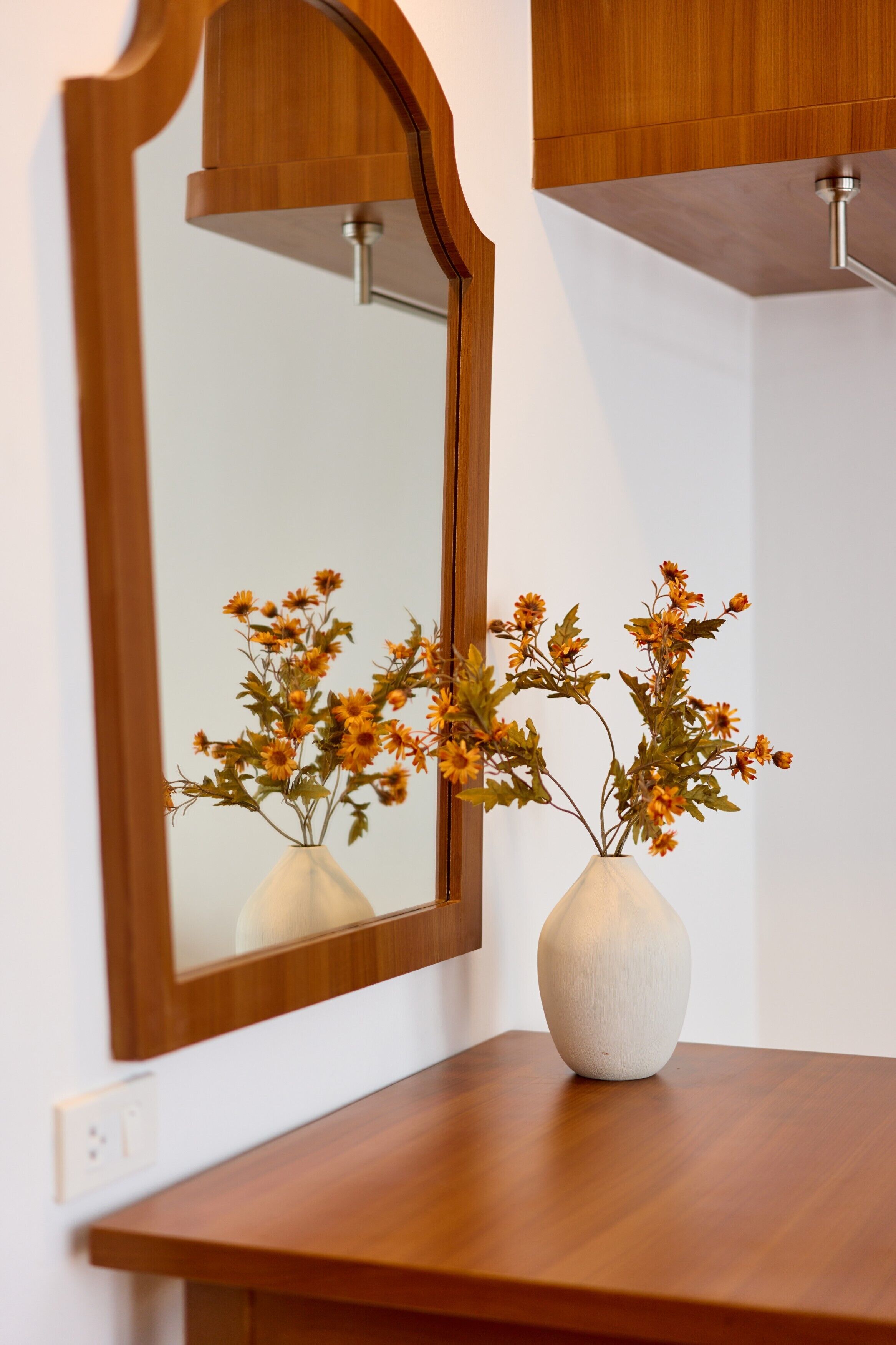 A wooden vanity with a mirror and two white vases with flowers.