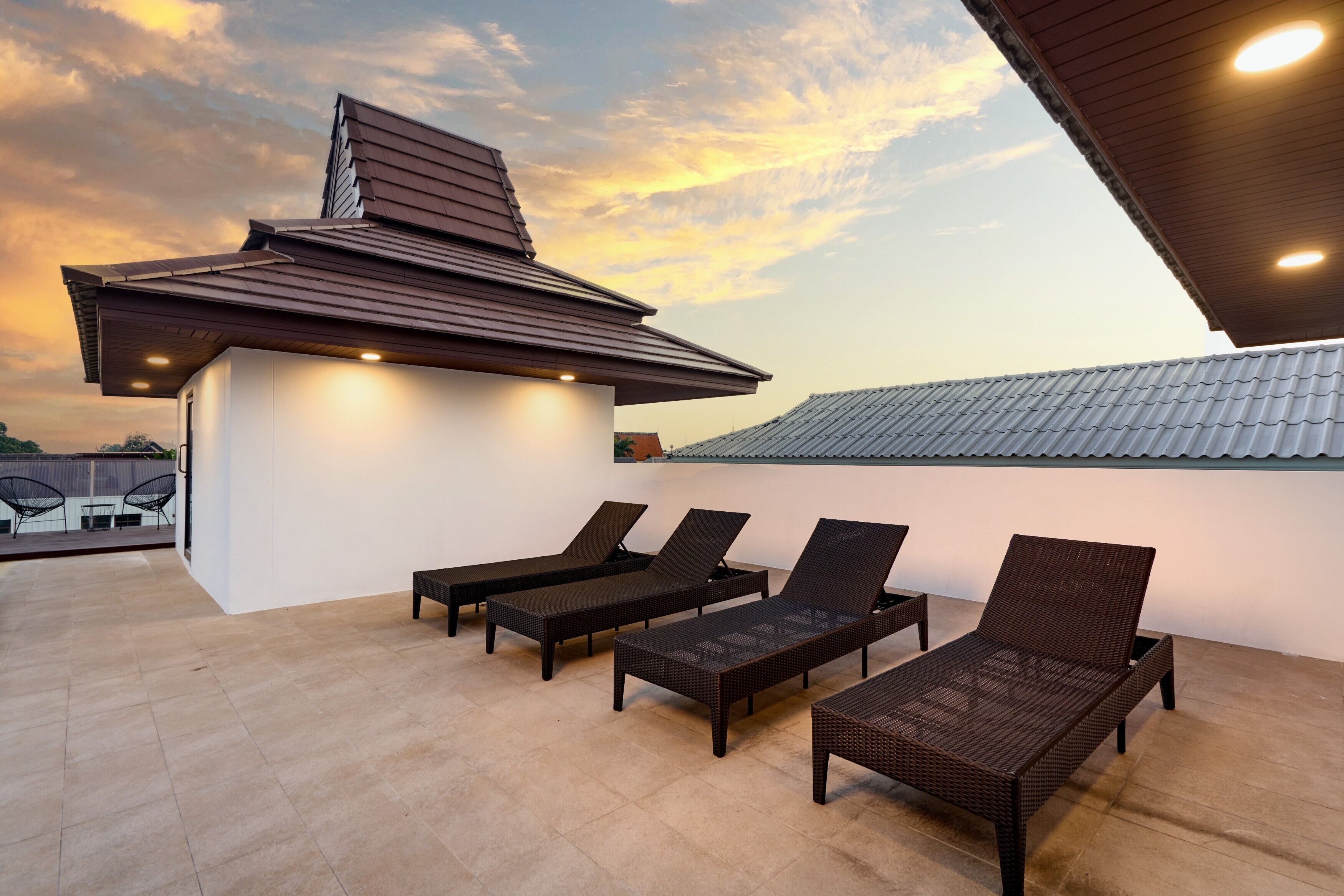 A rooftop terrace with four dark wicker lounge chairs and a small white structure with a slanted roof.