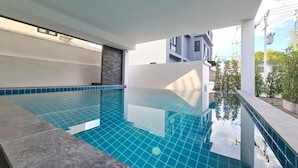 An indoor swimming pool with clear blue tiles, surrounded by a modern architectural design with white pillars and a stone accent wall. - Be Phrasingh Hotel Chiang Mai (Chiang Mai)