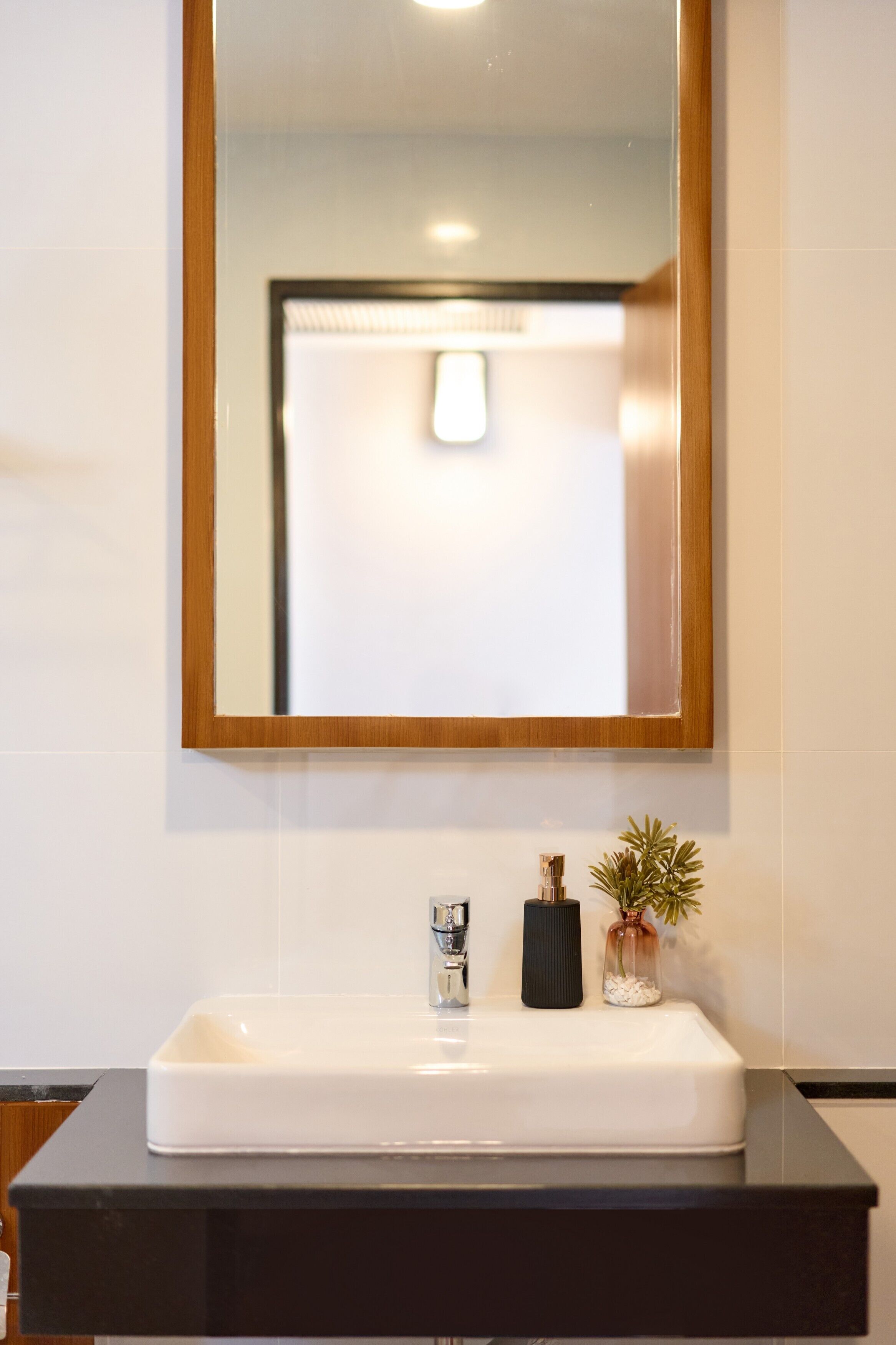 A bathroom with a white sink, a mirror with a wooden frame, and a small potted plant on the counter.