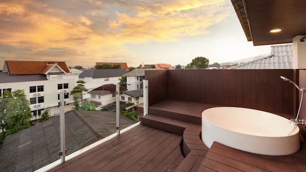 A rooftop terrace with a white bathtub and wooden deck, overlooking a residential area with houses and a temple. - Be Phrasingh Hotel Chiang Mai (Chiang Mai)
