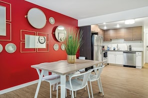 Een moderne keuken met houten kasten, een roestvrijstalen koelkast en een eethoek met een houten tafel en witte stoelen.
