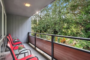 Een balkon met een rij rode stoelen en een plant in pot, met uitzicht op een dichtgroen bos.