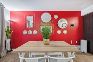 A dining area with a red wall, a wooden table, white chairs, and a potted plant. - Bellevue Way SE Executive Suite - Free Parking + WiFi - Monthly Stays (Bellevue)