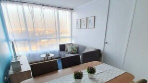 A modern living room with a wooden dining table, cushioned seating, and a large window with sheer curtains. - Beautiful apartment steps from the subway (Santiago)
