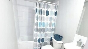 A small bathroom with a toilet, a bathtub, a shower curtain, a sink, and a mirror. - Beautiful apartment steps from the subway (Santiago)