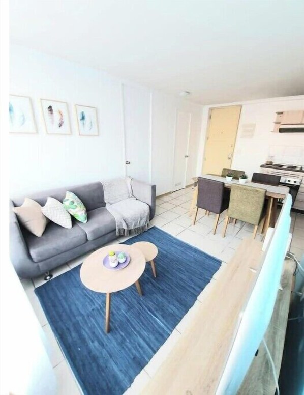A compact living space with a sofa, a small round table, and a kitchen area with a stove and chairs.