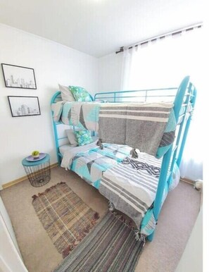 A small, cozy bedroom with a bunk bed, a small round side table, a woven rug, and two framed pictures on the wall.