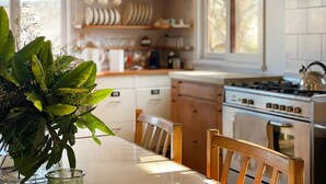 A kitchen with a white countertop, wooden chairs, and a stove. - Marguerite House by Free Trade Co (Braidwood)