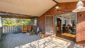 A covered deck with wooden flooring, outdoor seating, and a glass door leading to an interior space. - Marguerite House by Free Trade Co (Braidwood)