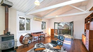 A spacious living area with a large fireplace, a dining table, leather chairs, and a view of the backyard through a glass door. - Marguerite House by Free Trade Co (Braidwood)