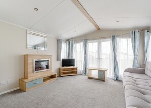 Un salon moderne doté d’un téléviseur à écran plat, de meubles en bois, d’un canapé et de grandes fenêtres avec des rideaux.