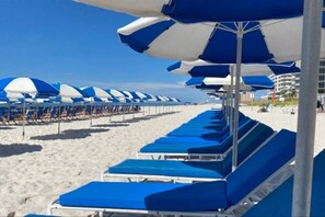 Ein Strand mit blauen Liegestühlen und weißen Sonnenschirmen.