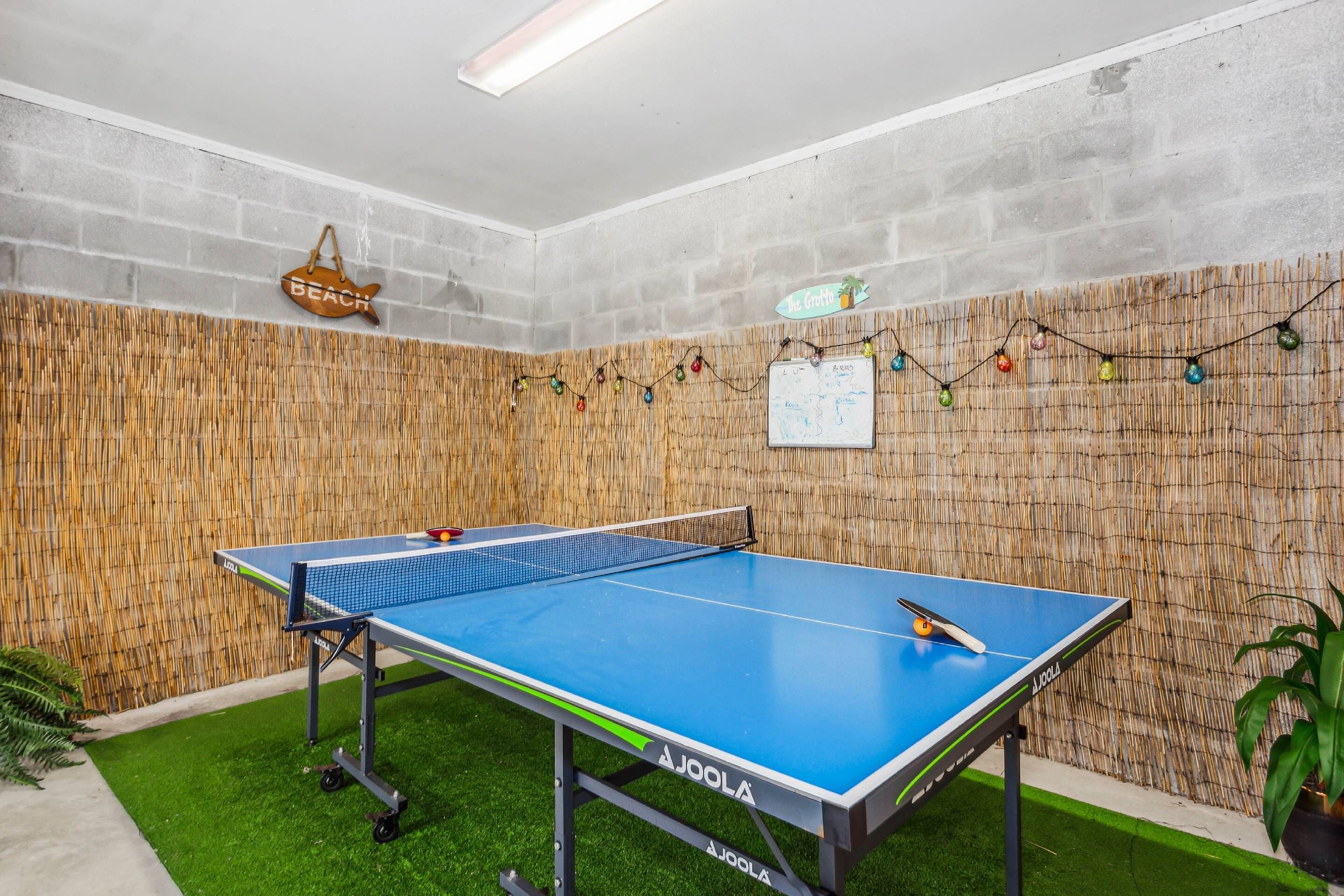 Ein Tischtennistisch mit Netz in einem Raum mit Backsteinwand, Holzwand und grünem Kunstgrashallenboden.