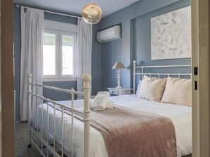 Une chambre à coucher avec un lit en métal blanc, une table de chevet avec une lampe et une fenêtre avec des rideaux blancs.