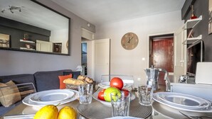 A modern living room with a dining area, featuring a sofa, a coffee table with fruit and glasses, and a kitchen visible in the background. - Live the charms of Seville in Triana (Sevilla)