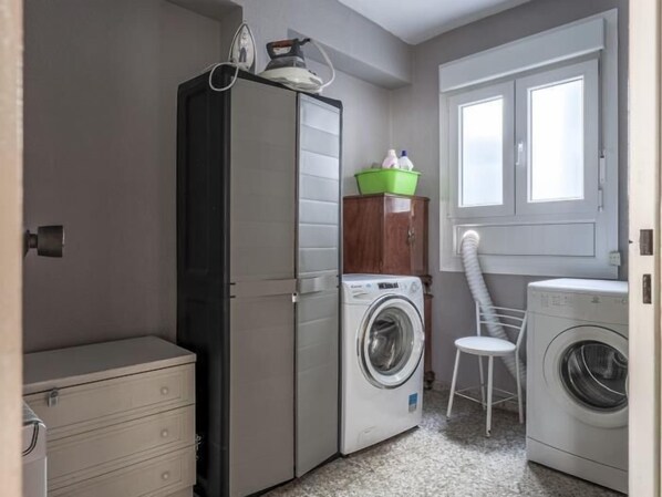 Une petite buanderie comprenant un lave-linge, un sèche-linge, un meuble de rangement et une chaise.
