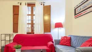 Un salon avec un canapé rouge, un canapé à carreaux, une petite table avec une plante et une lampe rouge.