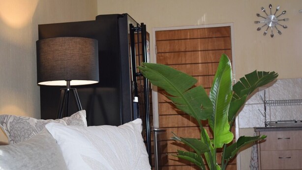 Un dormitorio con cama, lámpara, planta, armario de madera y un reloj de pared.