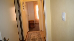 Un pasillo estrecho con un rug elaborado, una cesta de mimbre y una puerta que da a una habitación con cortina.