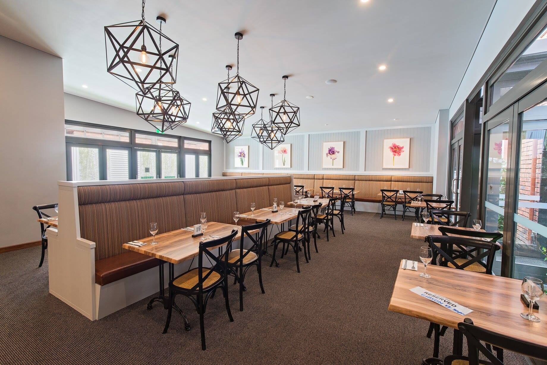 A restaurant with a long counter, booths, and a high ceiling with geometric pendant lights.