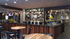 A modern bar area with wooden bar counters, hanging pendant lights, and a variety of bottles and glasses on shelves. - The George Hotel (Bathurst)