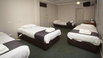 Habitación de hotel con tres camas, ventilador de techo, televisión y una mesita de noche con lámpara.