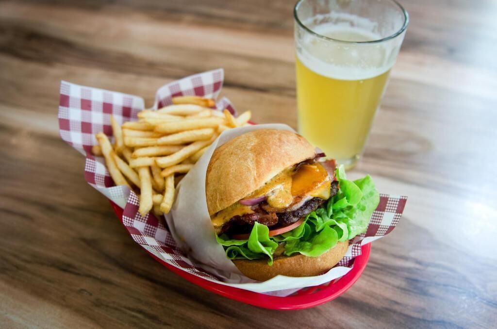 Hamburguesa con papas fritas y una cerveza en una mesa de madera.