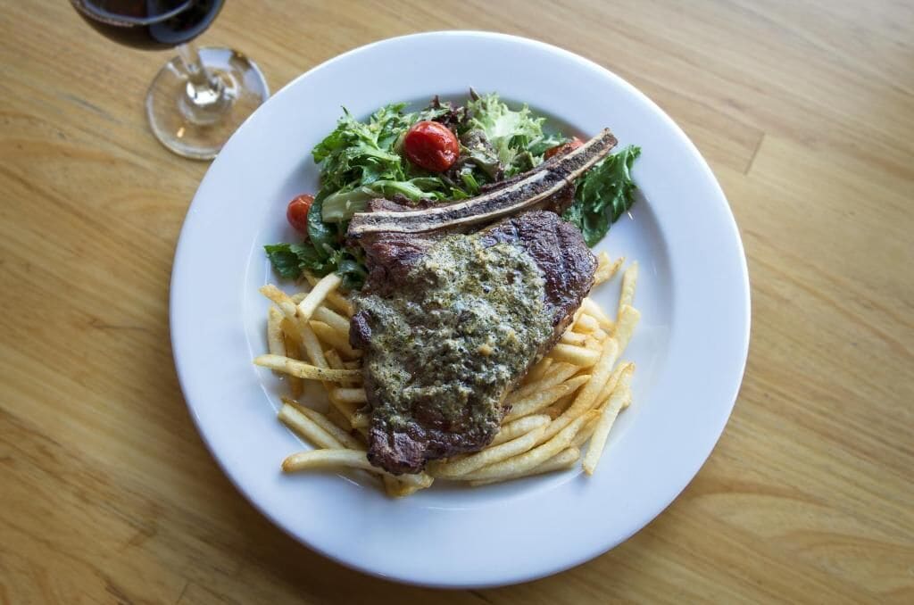 Un plato con un bistec, papas fritas y una ensalada sobre una mesa de madera.