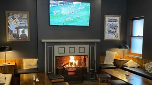 A cozy lounge area with a fireplace, comfortable seating, and a television mounted on the wall. - The George Hotel (Bathurst)