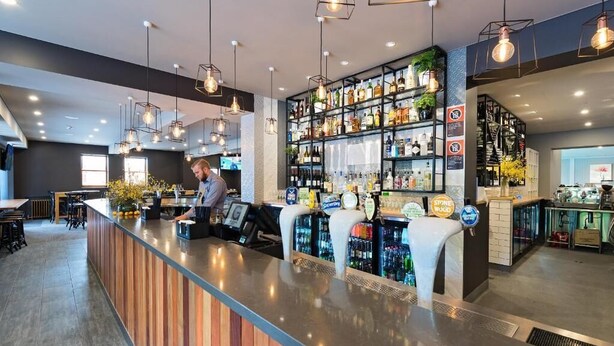 A bar area with a bartender, shelves of liquor bottles, and hanging light fixtures. - The George Hotel (Bathurst)