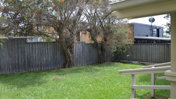 A backyard with a wooden fence, a tree, and a building in the background.