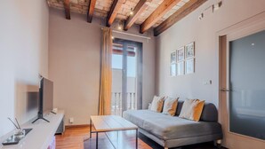 Ein modernes Wohnzimmer mit einer Couch, einem Fernseher, einem Tisch und einem Balkon.