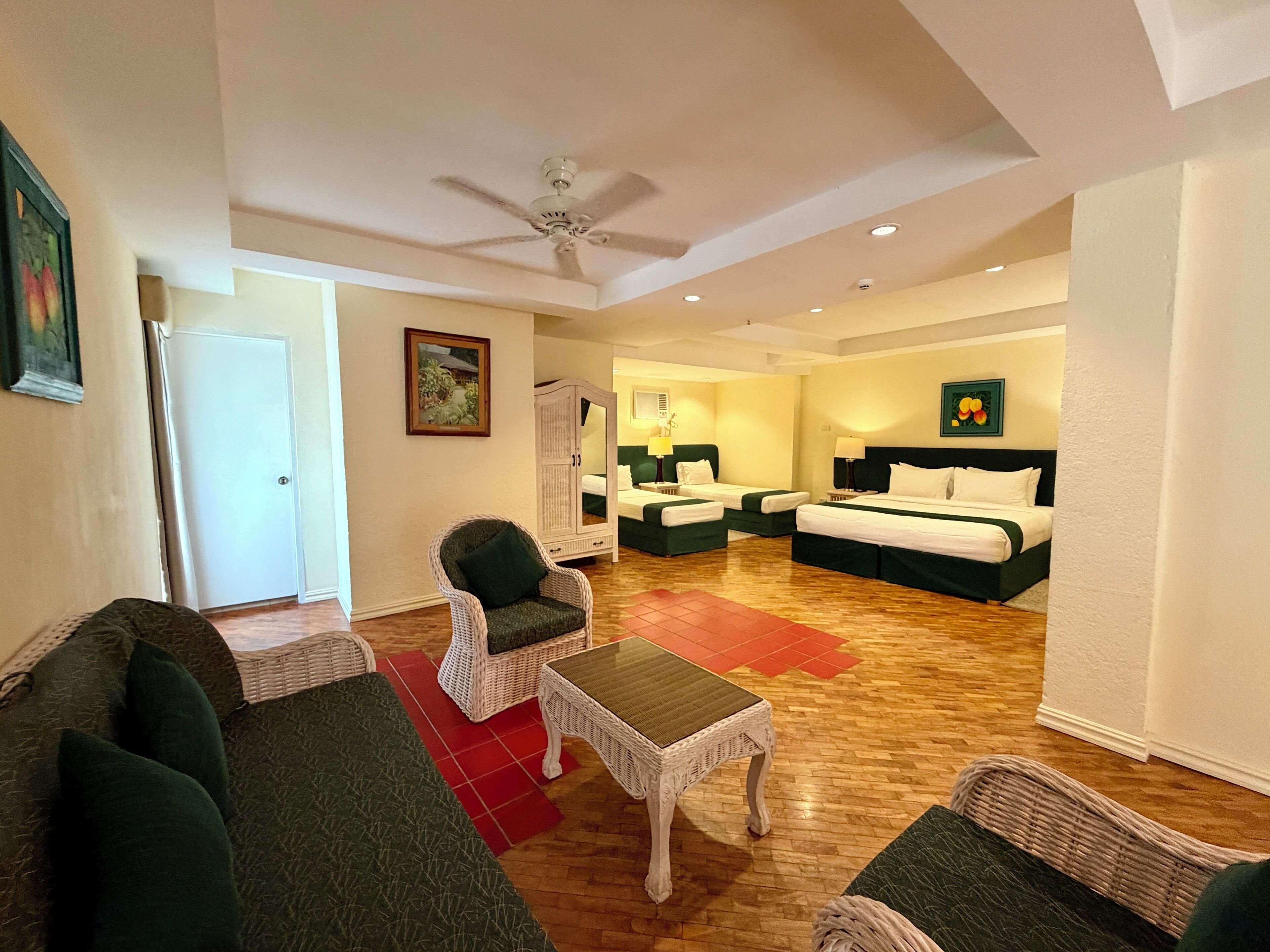 Une chambre d’hôtel comprenant un lit, deux tables de chevet, une chaise, une petite table, une armoire et un ventilateur de plafond.