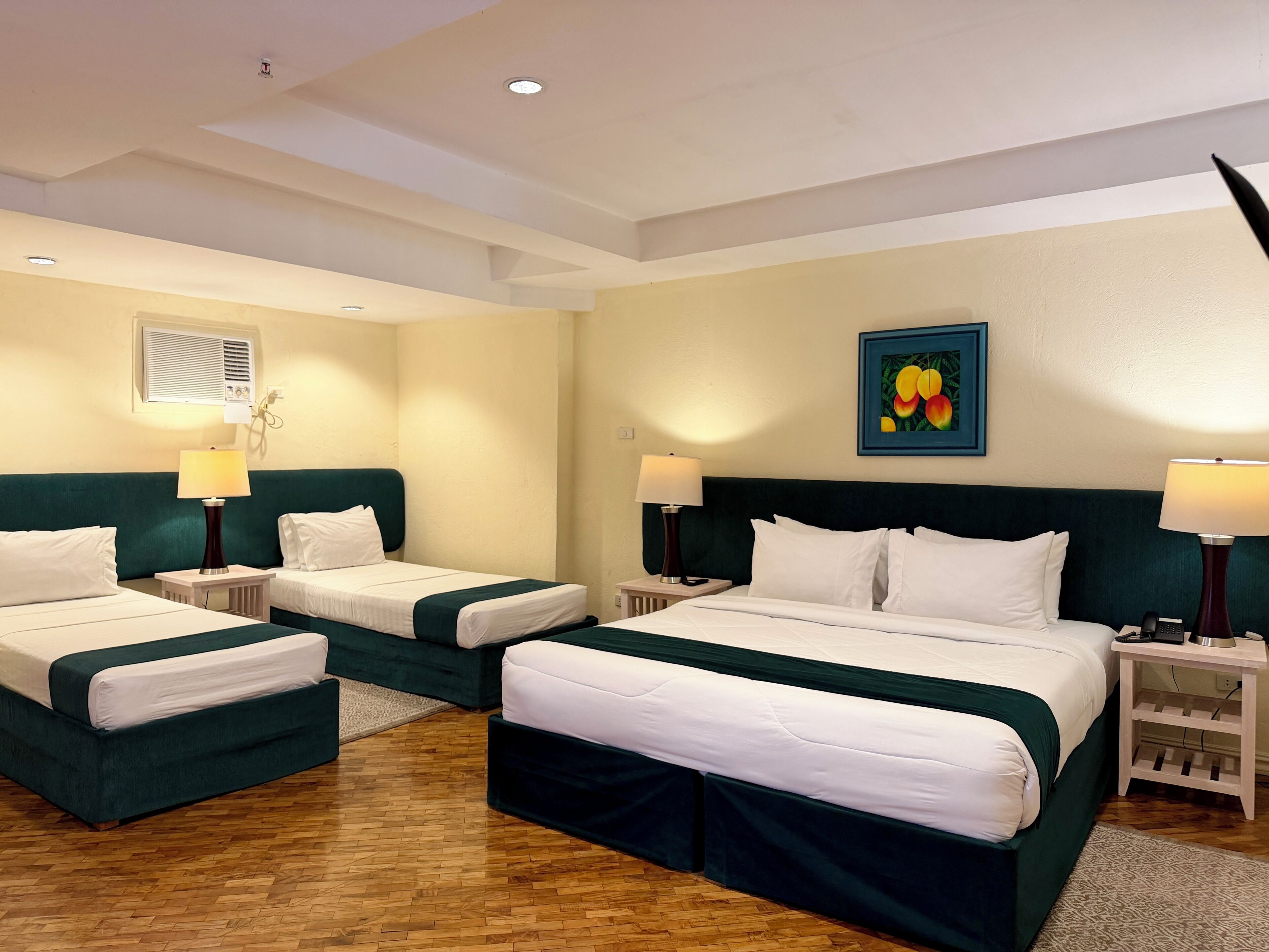 Une chambre d’hôtel avec deux lits, une petite table, une lampe, un tableau et un luminaire au plafond.