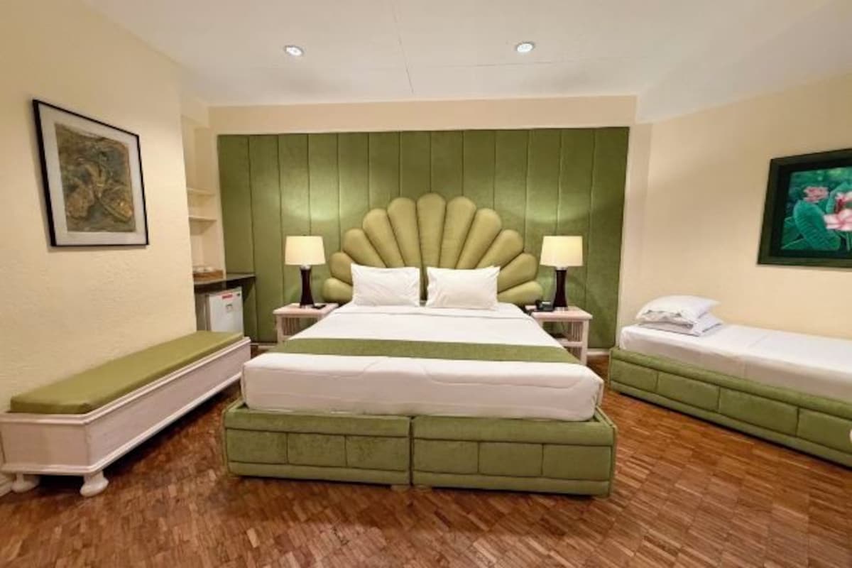 A hotel room with a large bed, two bedside tables with lamps, a bench, and a small sofa.