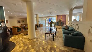A spacious lobby with a checkered floor, a large central column, and seating areas with sofas and a table. - Coco Grande Hotel (Dumaguete)