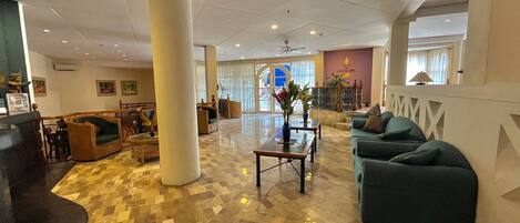 A spacious lobby with a checkered floor, a large central column, and seating areas with sofas and a table.