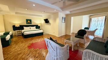 Habitación de hotel con cama, dos mesitas de noche, ventilador de techo, mesa de comedor y muebles de mimbre.
