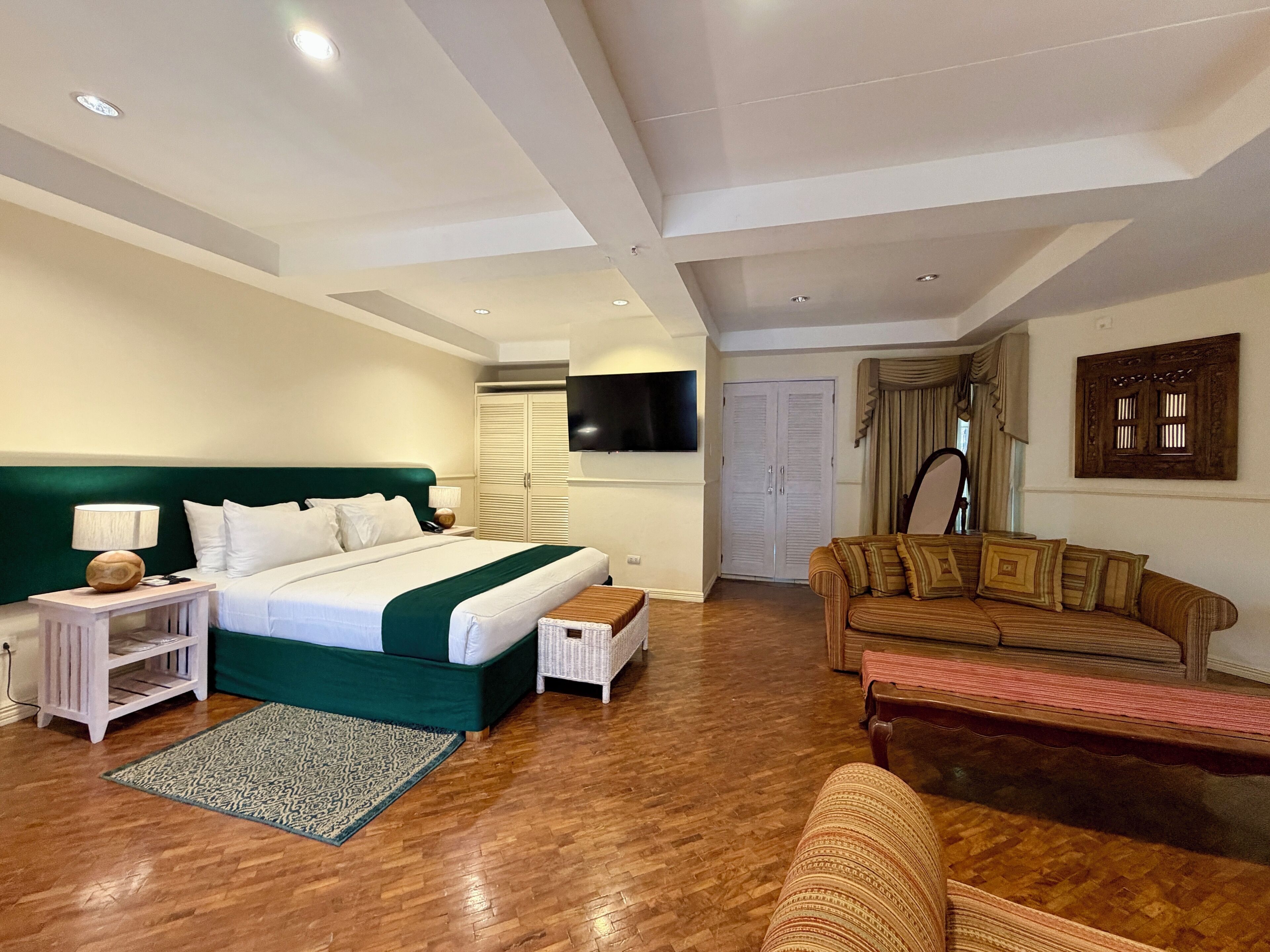 A hotel room with a bed, a sofa, a TV, a wardrobe, and a patterned rug.