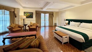 A hotel room with a large bed, two armchairs, a small table, and a bench. - Coco Grande Hotel (Dumaguete)