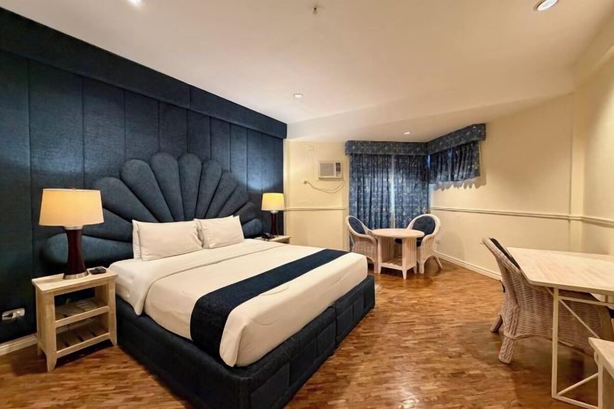 A hotel room with a large bed, two bedside tables, a small table with chairs, and a window with curtains.