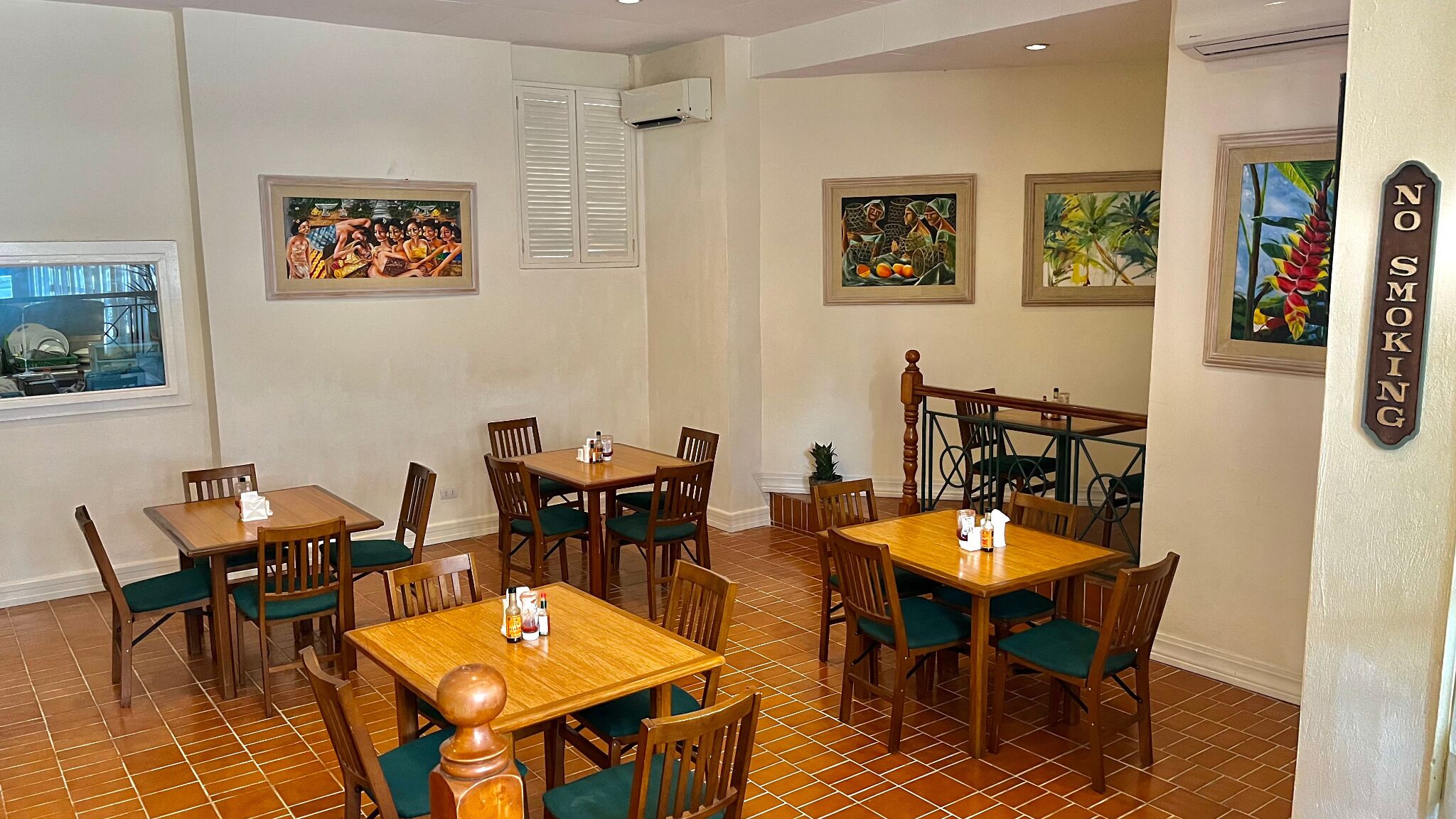 A dining area with wooden tables and chairs, air conditioning units, and tropical-themed wall art.