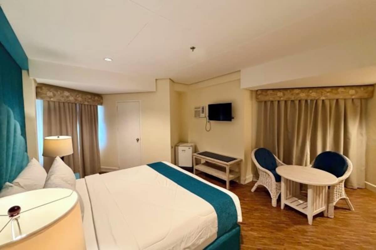 A hotel room with a bed, a desk, a chair, a TV, and curtains.
