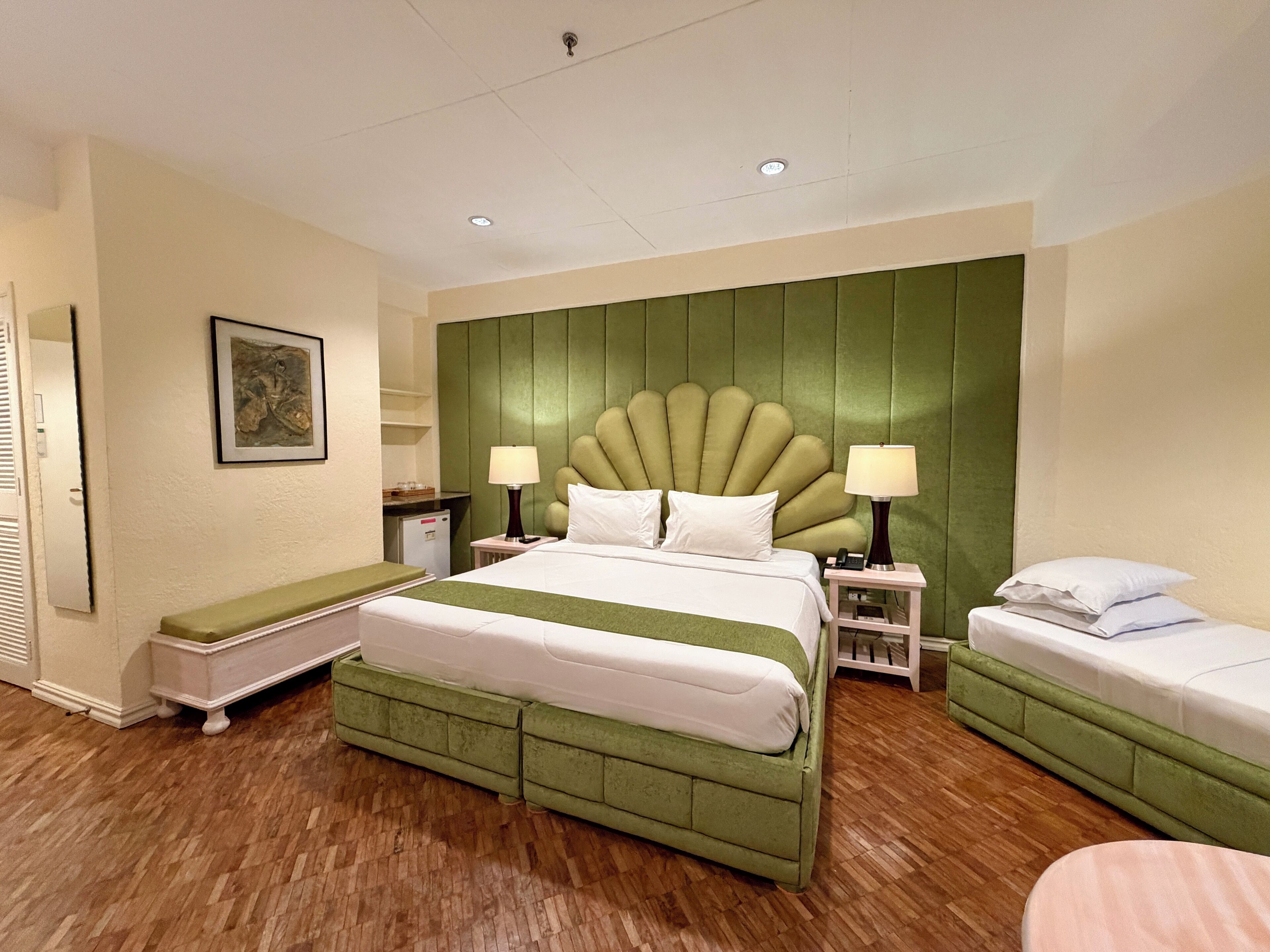 Quarto de hotel com cama grande, duas mesas de cabeceira, um banco e uma pequena escrivaninha.