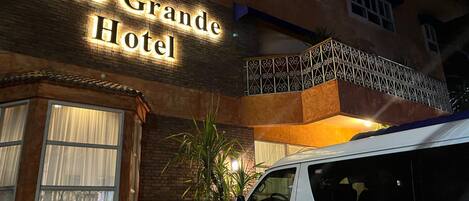 El Hotel Coco Grande con un letrero iluminado, una camioneta blanca estacionada al frente y un balcón con barandilla decorativa.