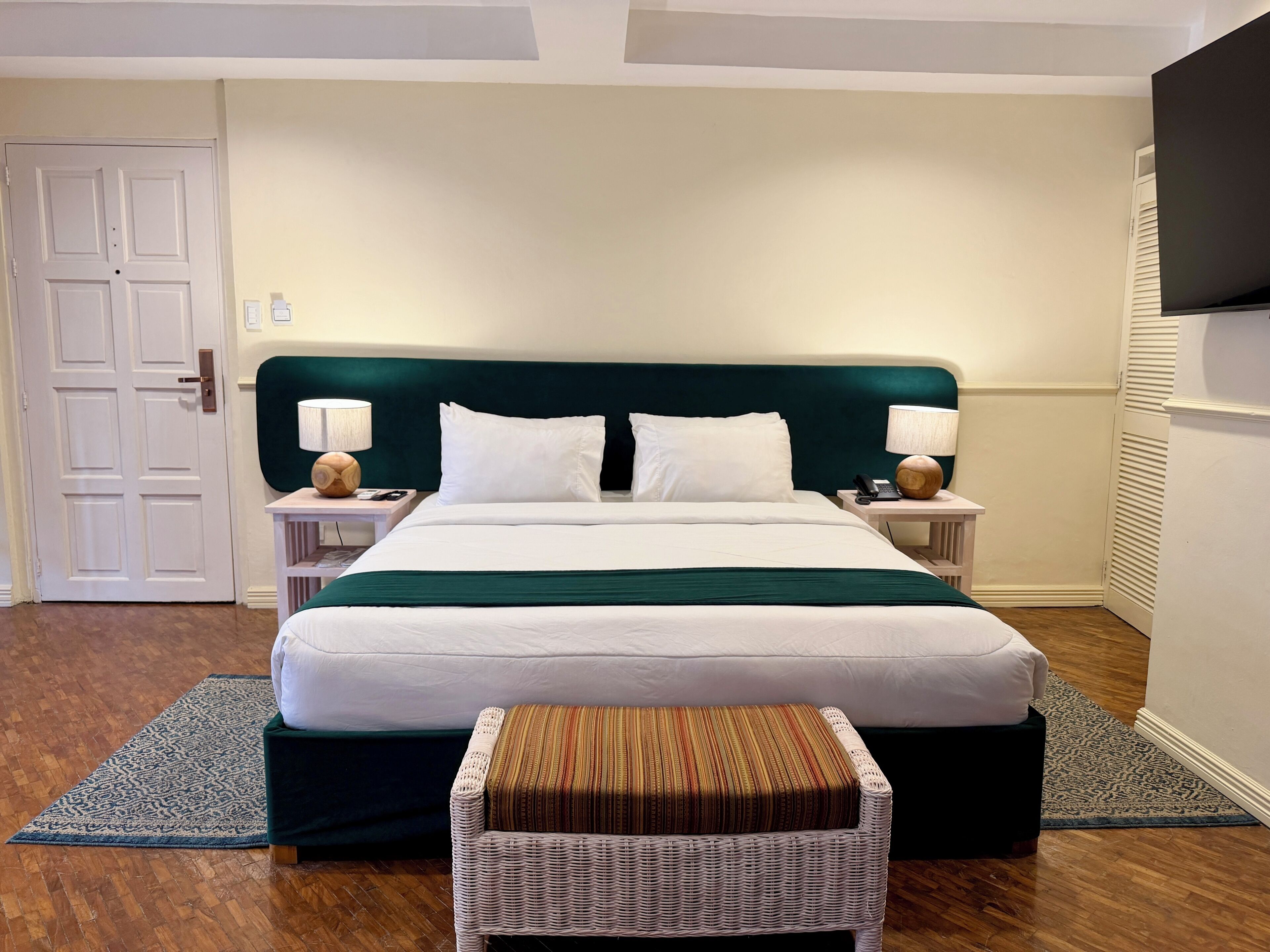 A hotel room with a bed, two bedside tables, a chair, a TV, and a door.