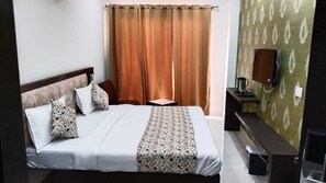 A neatly made bed with a patterned bedspread, a bedside table with a lamp, and a wall-mounted TV. - Hotel Bagga Kuteer (Haridwar)